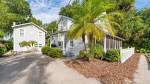 A two-story house with a porch and a small garden area with palm trees. - Historic Tremain  Cottages (Mount Dora)