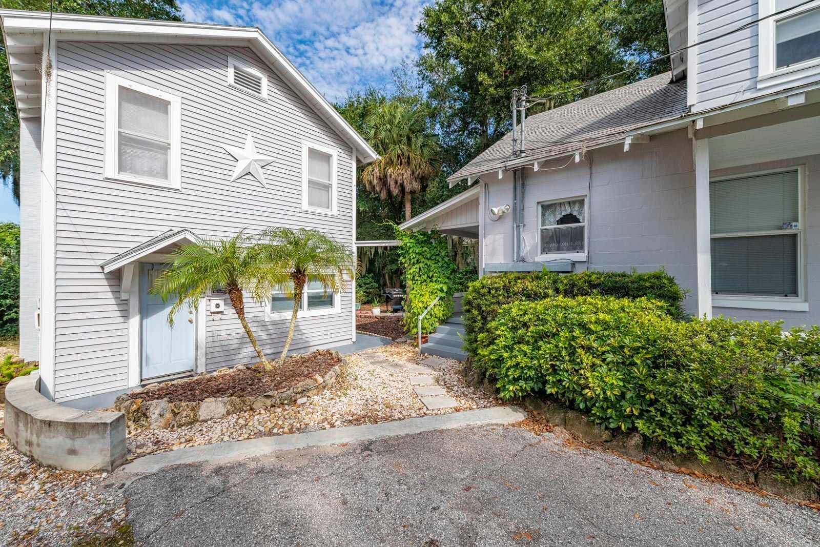 A two-story house with a small porch, a star decoration, and a well-maintained garden with palm trees and shrubs.