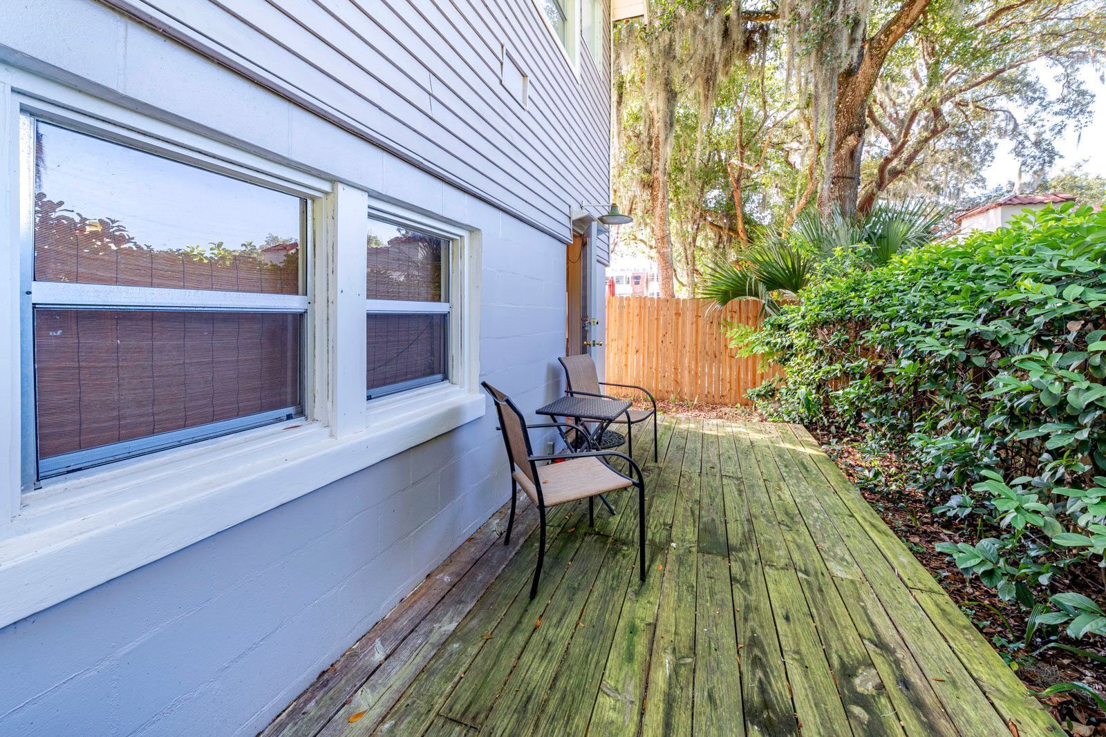 A wooden deck with two chairs and a table, a white building with large windows, and a wooden fence.