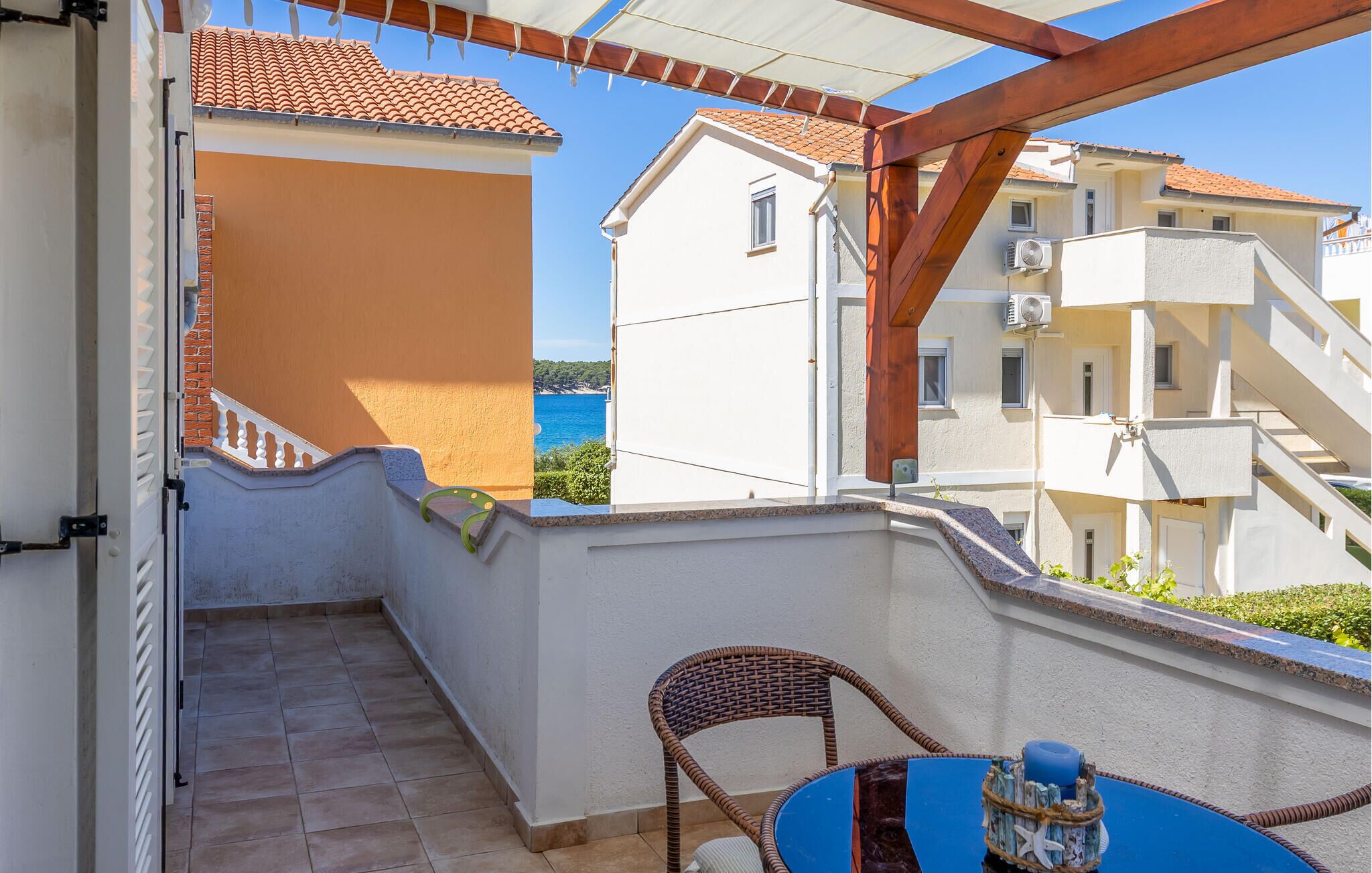 A balcony with a view of the sea, a wicker chair, and a table with a blue tablecloth.