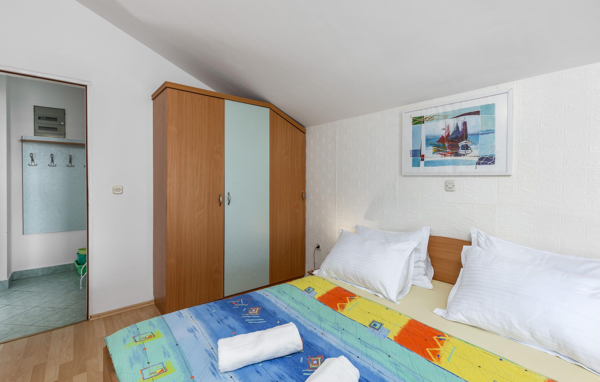 Habitación de hotel con cama, armario de madera, baño con espejo y un cuadro en la pared.