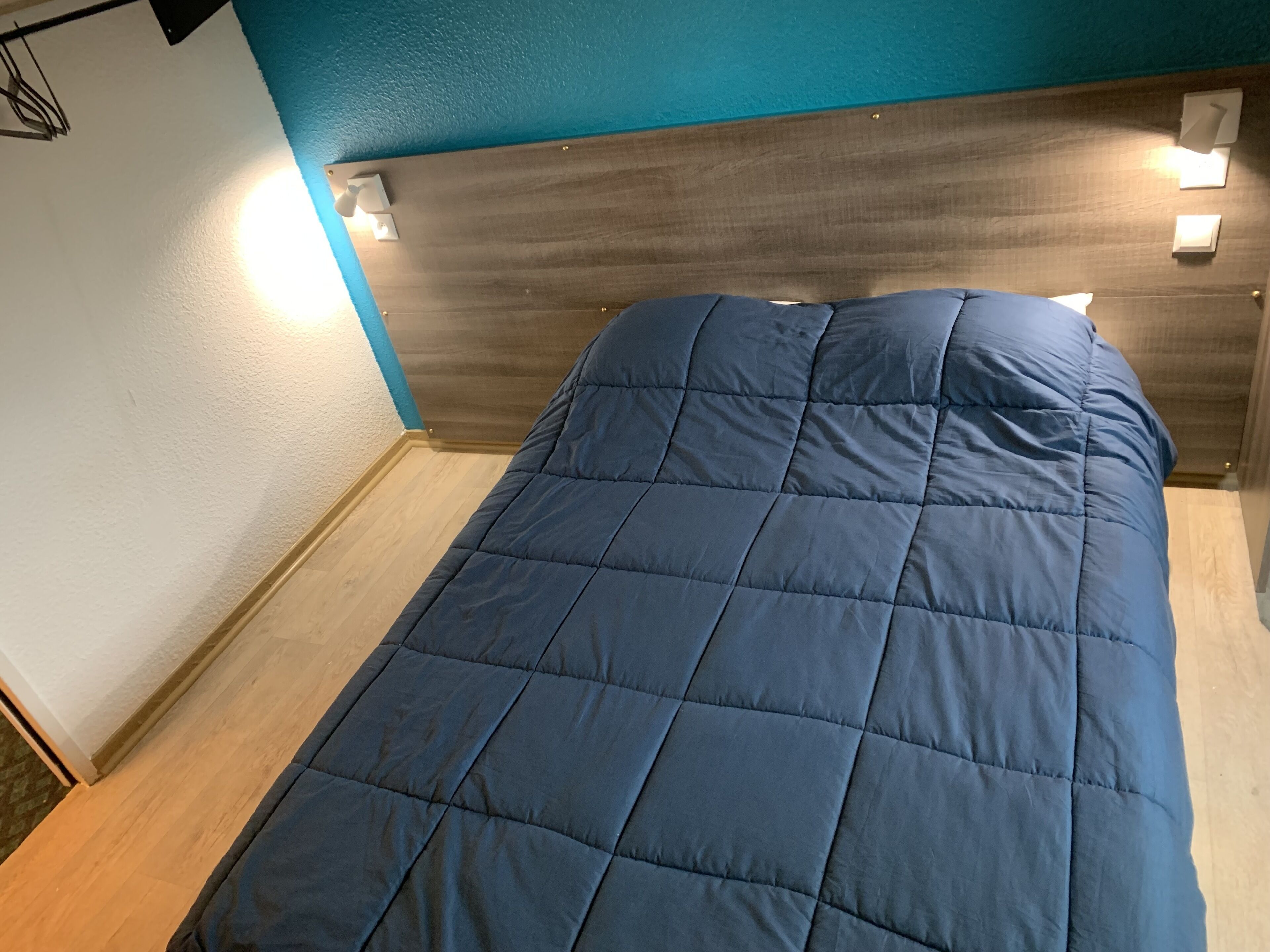 A bed with a blue quilt in a room with teal walls and wooden flooring.