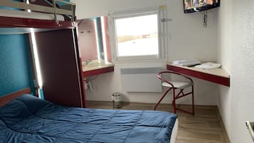 Ein kleines Zimmer mit Etagenbett, Schreibtisch mit Stuhl, Fenster und Wandfernseher.