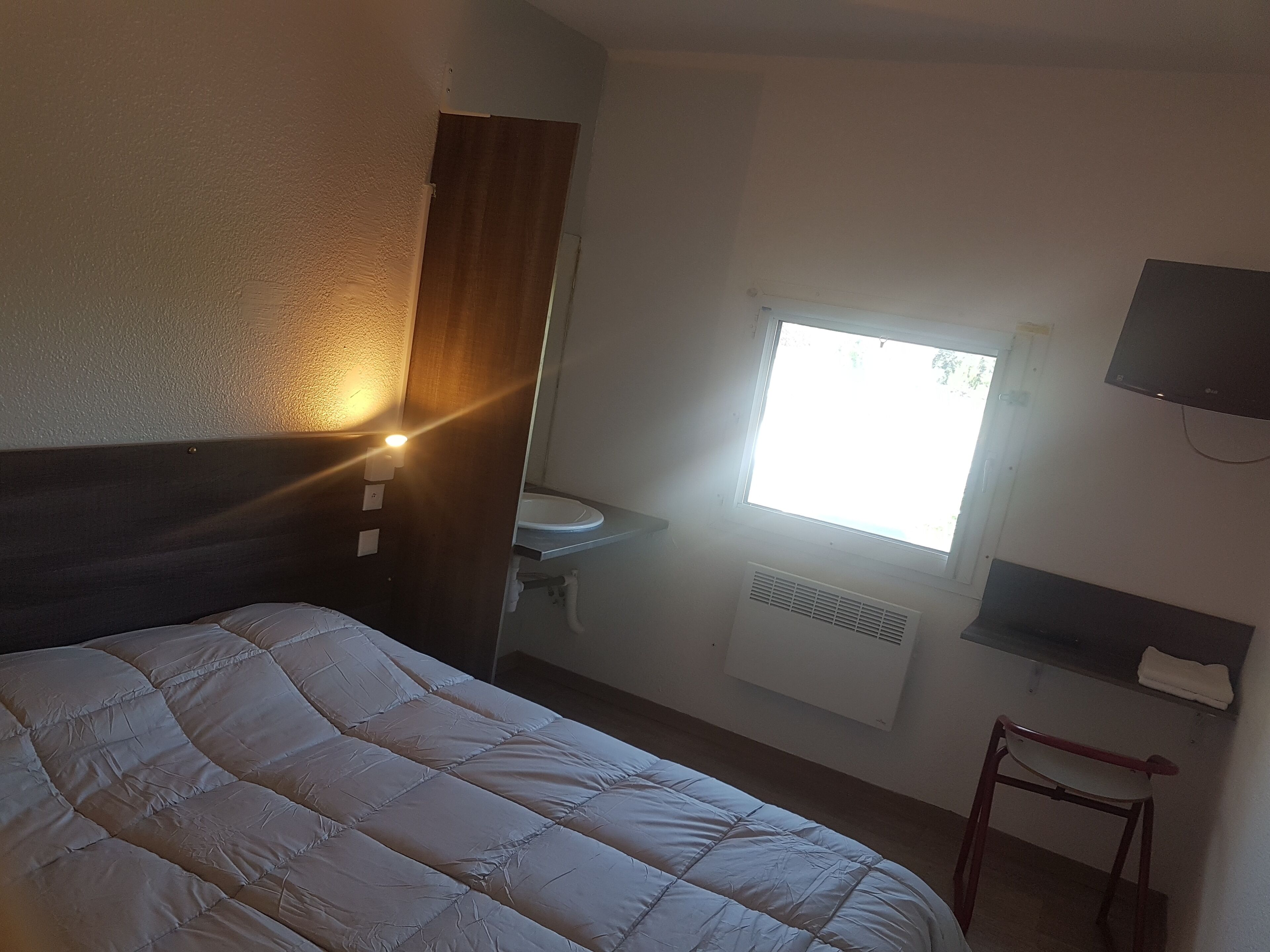 Una habitación de hotel con cama, ventana, lavamanos y televisión.