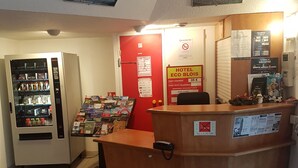 A hotel reception area with a red door, a vending machine, and a wooden counter with a phone.