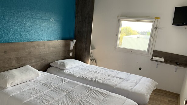 A room with two beds, a window, a TV, and a wooden headboard.