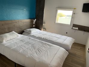 Una habitación con dos camas, una ventana, un televisor y un cabecero de madera.