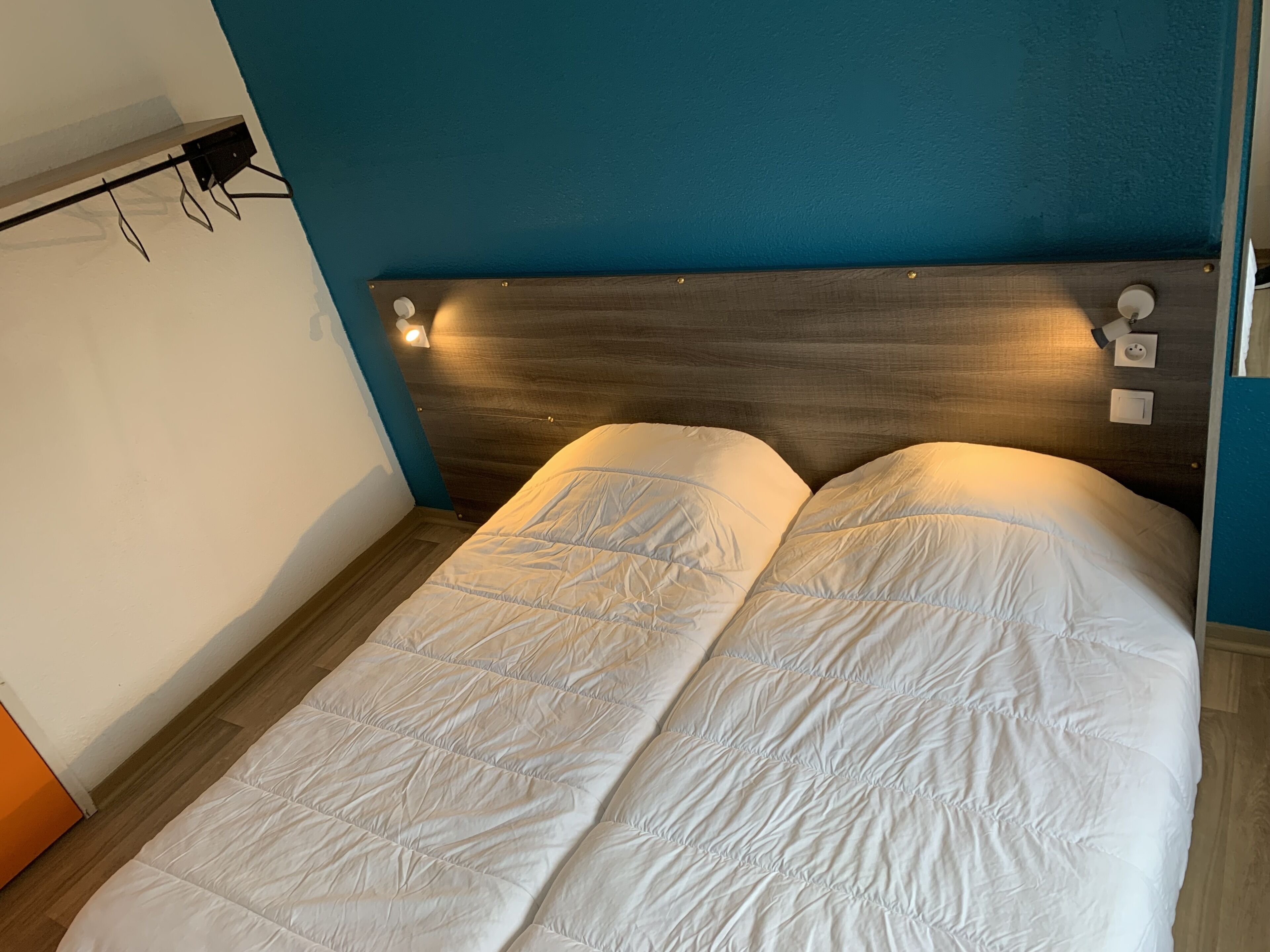 Uma cama de casal com cabeceira de madeira e duas luminárias de cabeceira.