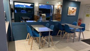 A restaurant interior with blue chairs and tables, a counter with a menu, and a view of the outside.