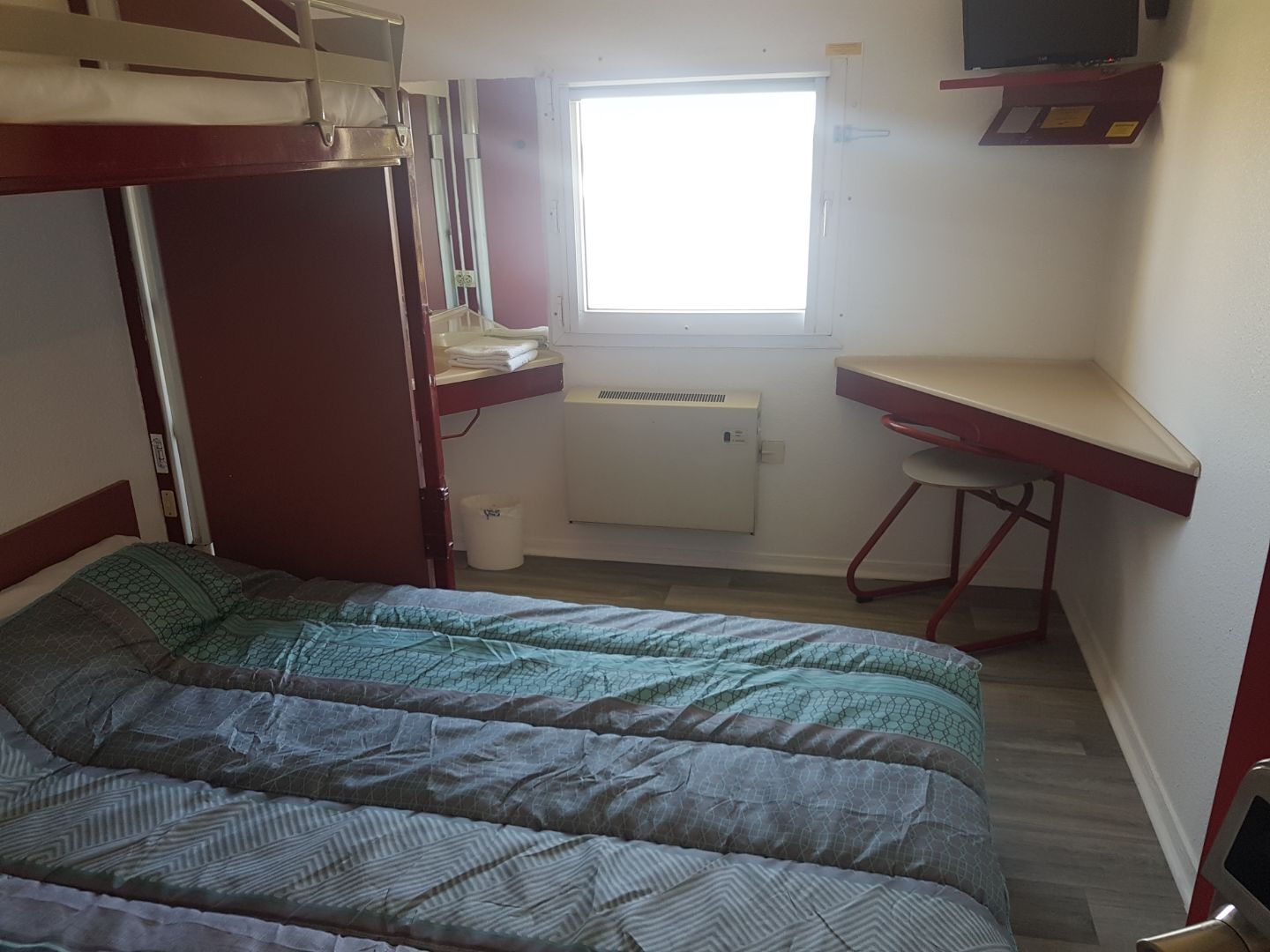 Un dormitorio con literas, un escritorio, una silla, un radiador y una ventana.