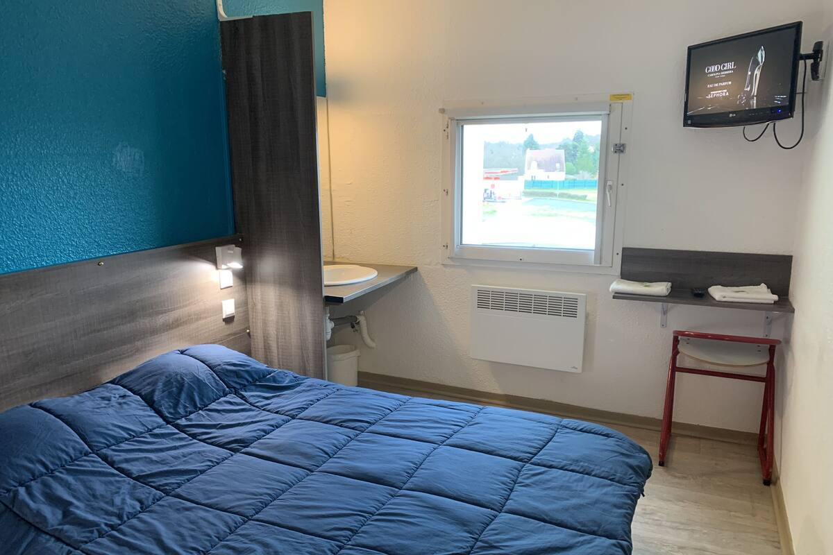 Hotelkamer met een bed, raam, wastafel, spiegel, televisie en een klein tafeltje met handdoeken.