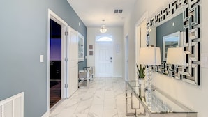 A hallway with a marble floor, a glass console table with a lamp, and a decorative mirror on the wall. - Imperial Retreat: Games,Pool,Theatre + Free Night (Champions Gate)