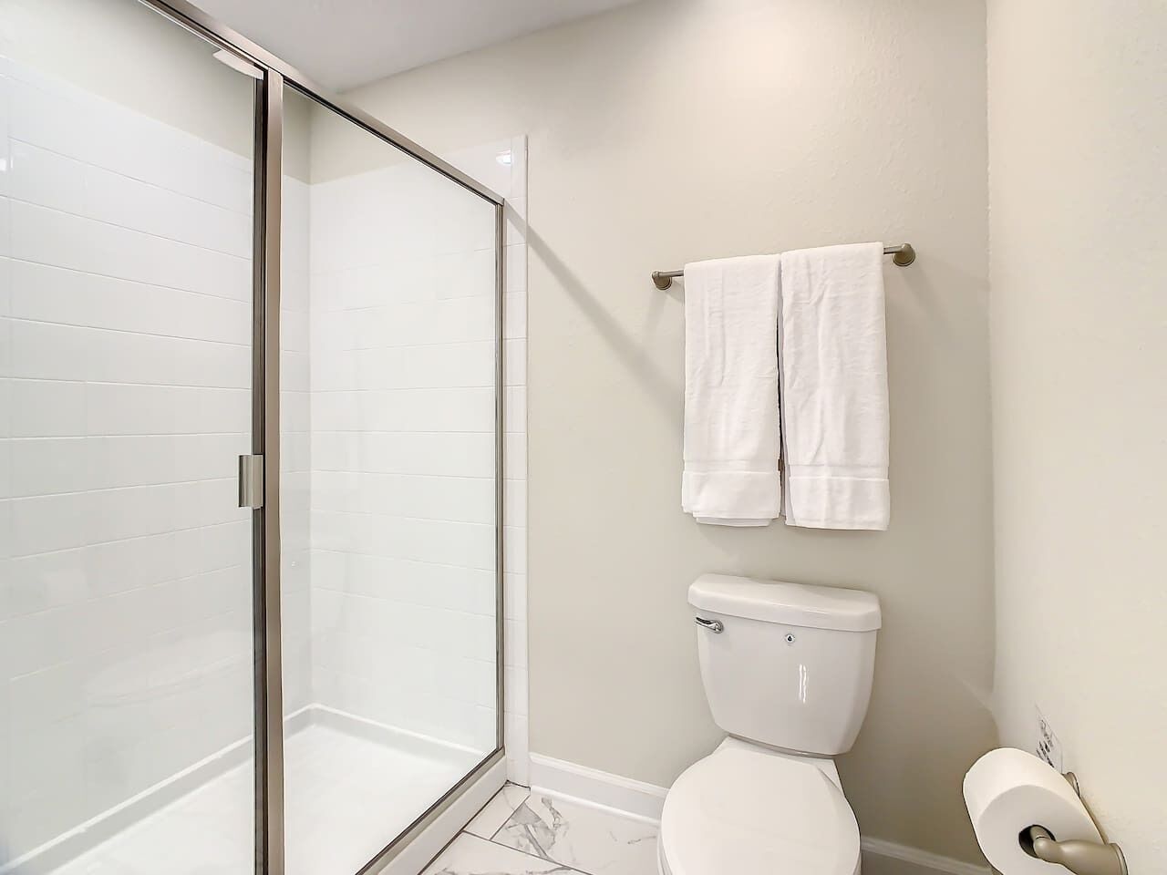 A bathroom with a glass shower enclosure, a toilet, and a towel rack with two towels.