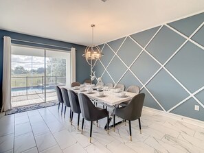 Een eetkamer met een grote tafel voor zes personen, een kroonluchter en uitzicht op een zwembad door grote ramen.