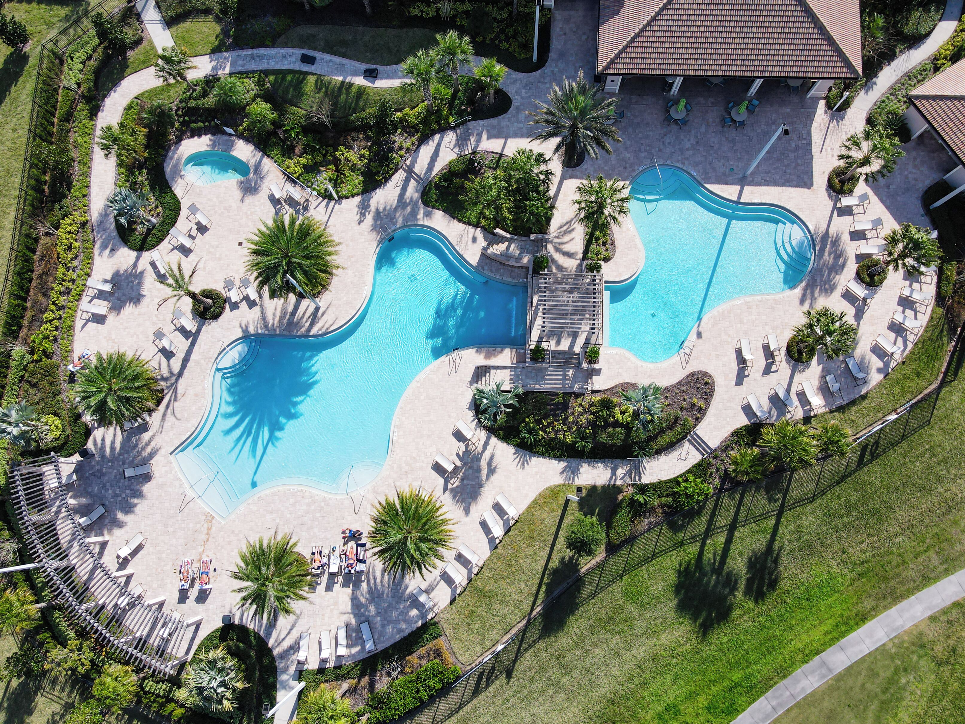 An aerial view of a resort with a large central pool, surrounded by sun loungers and palm trees.