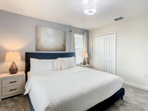 Een slaapkamer met een bed, twee nachtkastjes, een raam met jaloezieën, een deur en een plafondlamp.