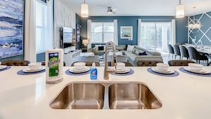 A modern kitchen with a central island, stainless steel sinks, and a dining area with a table set for four. - Imperial Retreat: Games,Pool,Theatre + Free Night (Champions Gate)