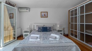 Ein Schlafzimmer mit einem großen Bett, zwei Nachttischen, einem kleinen Tisch, einer Heizung und einer Schiebetür aus Glas.
