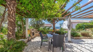 Eine möblierte Terrasse im Freien, umgeben von Grün und mit Blick aufs Meer.