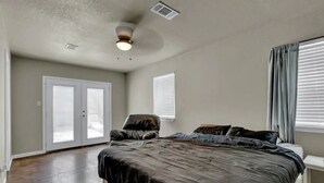 Ein Schlafzimmer mit einem großen Bett, einem Deckenventilator, einem Sessel und einem Fenster mit Jalousien.