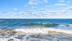 Ein Strand mit brechenden Wellen am Ufer unter einem teilweise bewölkten Himmel.