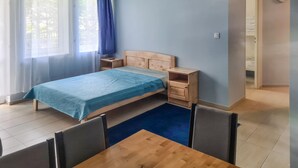 Ein Schlafzimmer mit Bett, Nachttischen, einem Sessel, einem kleinen Tisch und einem Fenster mit Vorhängen.