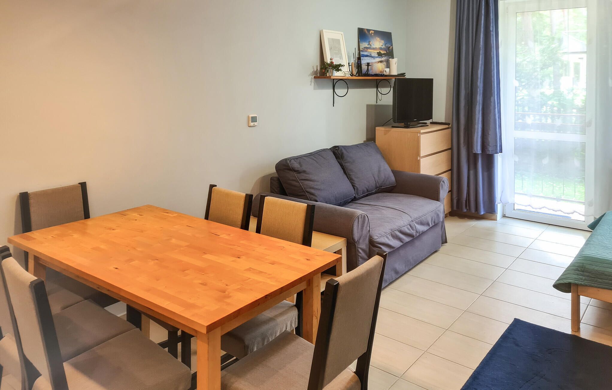 Una sala de estar con una mesa de comedor de madera, un sofá gris y un televisor sobre un mueble.