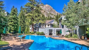 Ein Pool mit Liegestühlen und Sonnenschirmen, umgeben von Bäumen und einem Berg im Hintergrund.