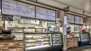 Eine Bäckerei mit mehreren Auslagen voller Backwaren, einer Kaffeemaschine und einer Speisekarte über der Theke.