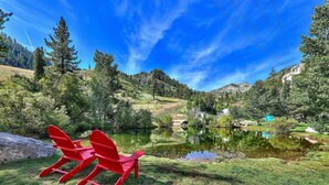 Ein friedlicher See mit roten Adirondack-Stühlen und freiem Blick auf den umliegenden Wald und die Hügel.