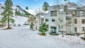Eine zweistöckige Lodge mit einer Seilbahn im Hintergrund, umgeben von schneebedeckten Bäumen und einer Bergkulisse.
