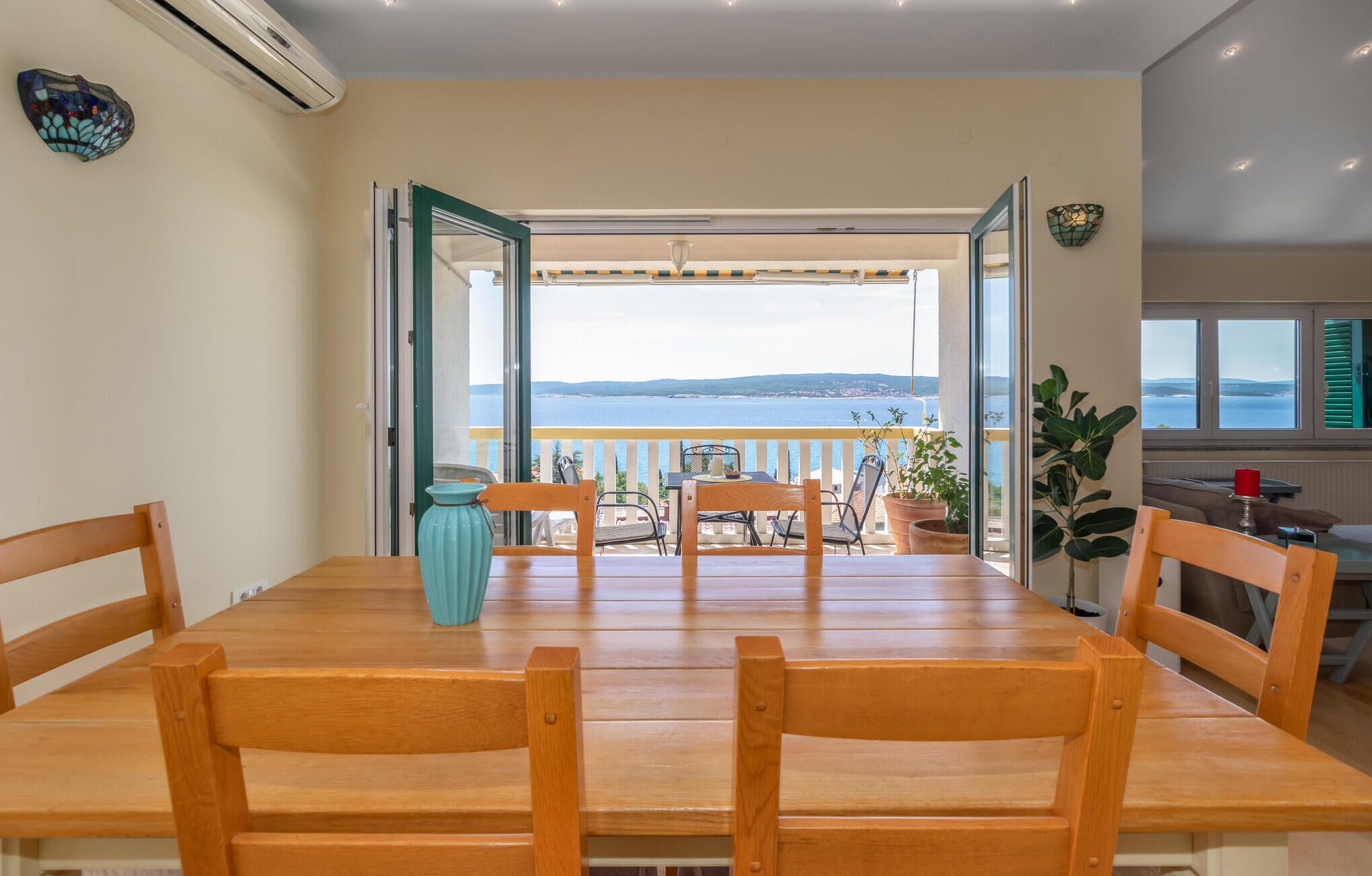 A dining area with a view of the sea, wooden furniture, and a vase on the table.