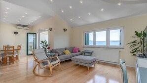 A spacious living area with a wooden floor, a grey sectional sofa, a rocking chair, and a dining table with chairs. - Lovely apartment in Crikvenica (Crikvenica)