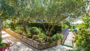 A stone pathway leading through a lush garden with various plants and a metal gate. - Lovely apartment in Crikvenica (Crikvenica)
