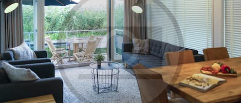 Een moderne woonkamer met een bank, stoelen, een eettafel en een balkon met uitzicht op groen.