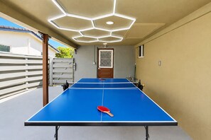 Una mesa de ping pong con una paleta, una lámpara de techo hexagonal y una puerta con un panel decorativo.