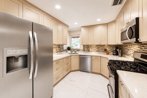 Una cucina moderna con elettrodomestici in acciaio inossidabile, mobili beige e una parete piastrellata.