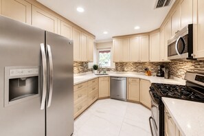 Une cuisine moderne dotée d’appareils électroménagers en acier inoxydable, de meubles de couleur beige et d’un pare-feu en carrelage.