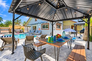 Un espace extérieur abrité comprenant une piscine, des chaises longues et une table agrémentée de verres colorés.