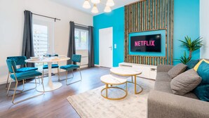 A modern living room with a dining area, a TV mounted on a blue wall, and a wooden slat design. - Le Moja Tourcoing (Tourcoing)