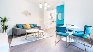 A modern living room with a grey sofa, blue chairs, a round white table, and a kitchen in the background. - Le Moja Tourcoing (Tourcoing)