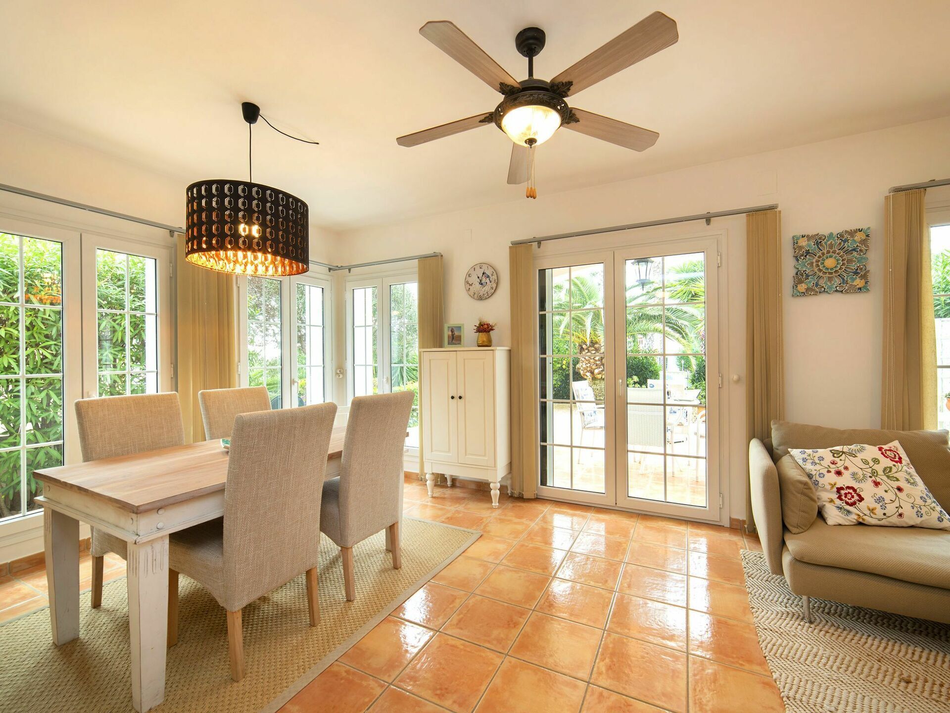 Une pièce spacieuse comprenant une table à manger, des chaises, un ventilateur de plafond et de grandes fenêtres.