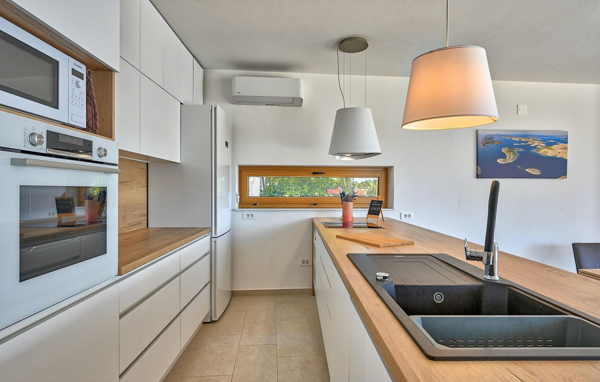 Una cocina moderna con horno empotrado, microondas y refrigerador. Hay un ventanal que proporciona luz natural y vistas al exterior.