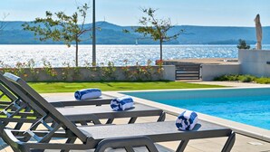 A poolside area with lounge chairs and towels, a view of the sea, and a statue. - Beautiful home in Turanj (Turanj)