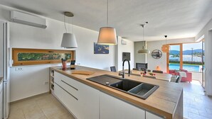 A modern kitchen with a central island, pendant lights, and a view of a pool. - Beautiful home in Turanj (Turanj)