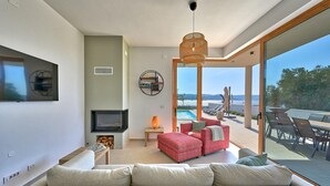 A modern living room with a large sofa, a TV, a fireplace, and a view of the sea through large windows. - Beautiful home in Turanj (Turanj)