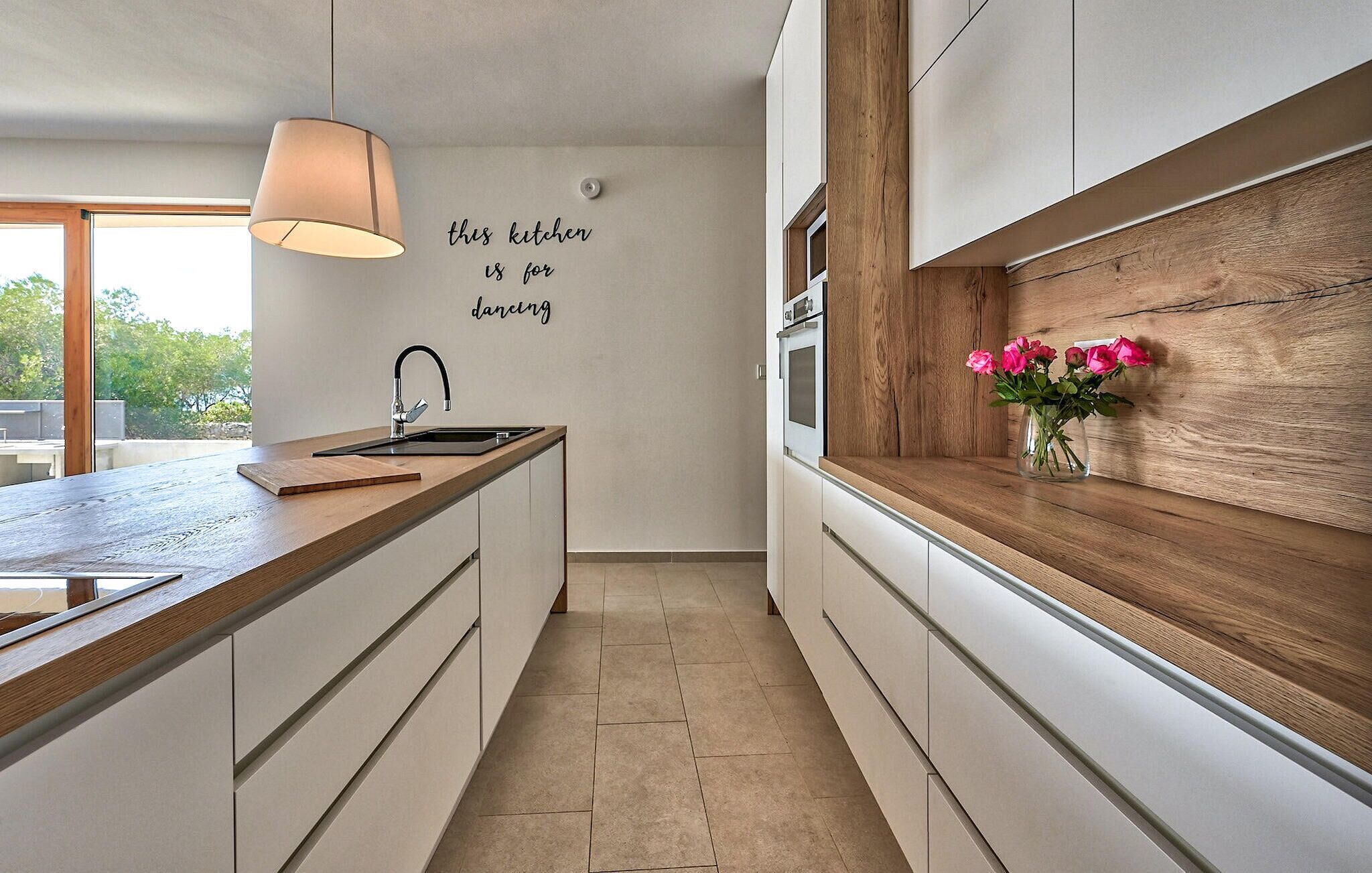 Una cocina moderna con encimera de madera, horno empotrado e iluminación fijada a la pared.