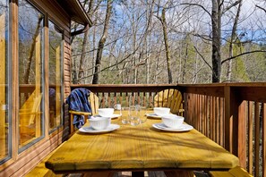 A wooden deck with a table set for four, surrounded by a forest. - Family Favorite! Arcade Games, Hot Tub, Rooftop Views, Great Gatlinburg Location (Gatlinburg)