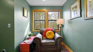 Una habitació amb una poltrona de pell, un escriptori amb estovall de color vermell, una làmpada i quadres a les parets.