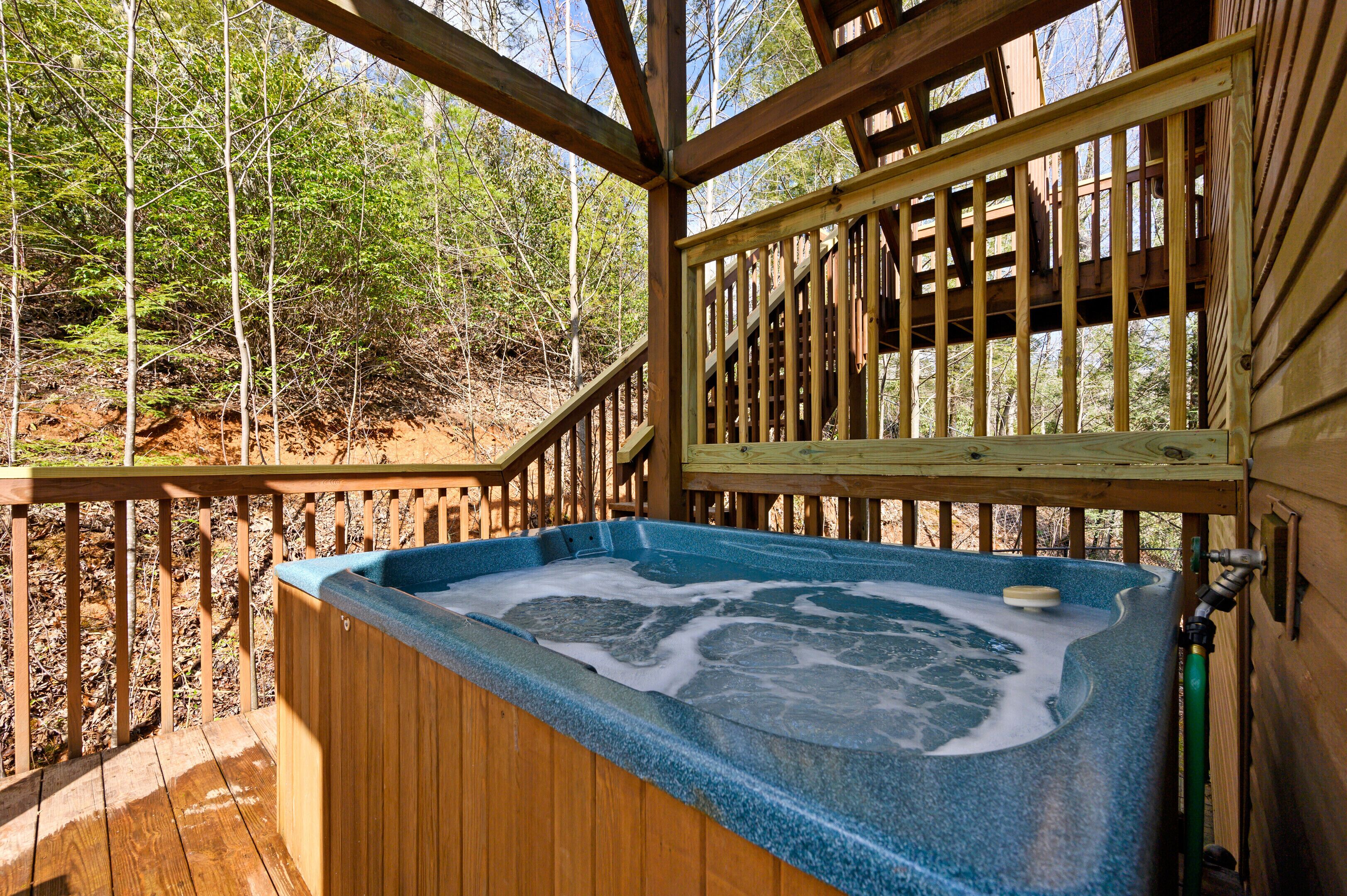 A wooden deck with a hot tub, surrounded by trees.